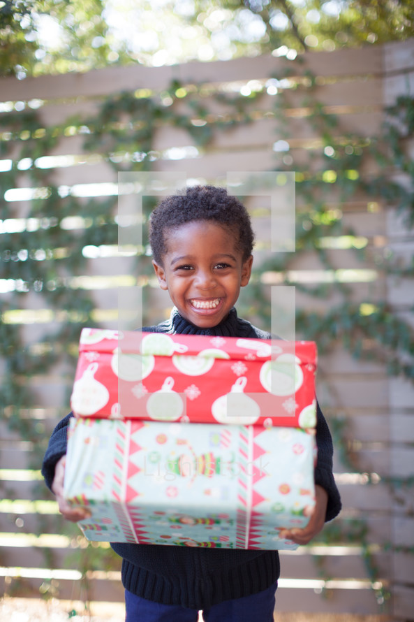 a boy child holding stacked Christmas gifts 