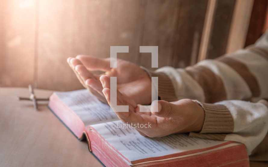 lifted praying hands over a Bible 