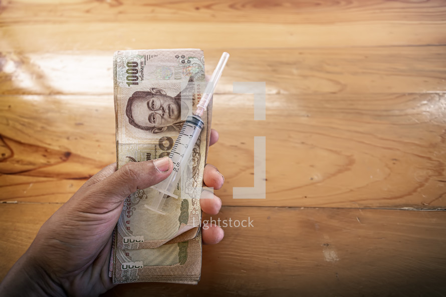 Close up Syringe,mask with Thai money in hand, Treatment that requires money.