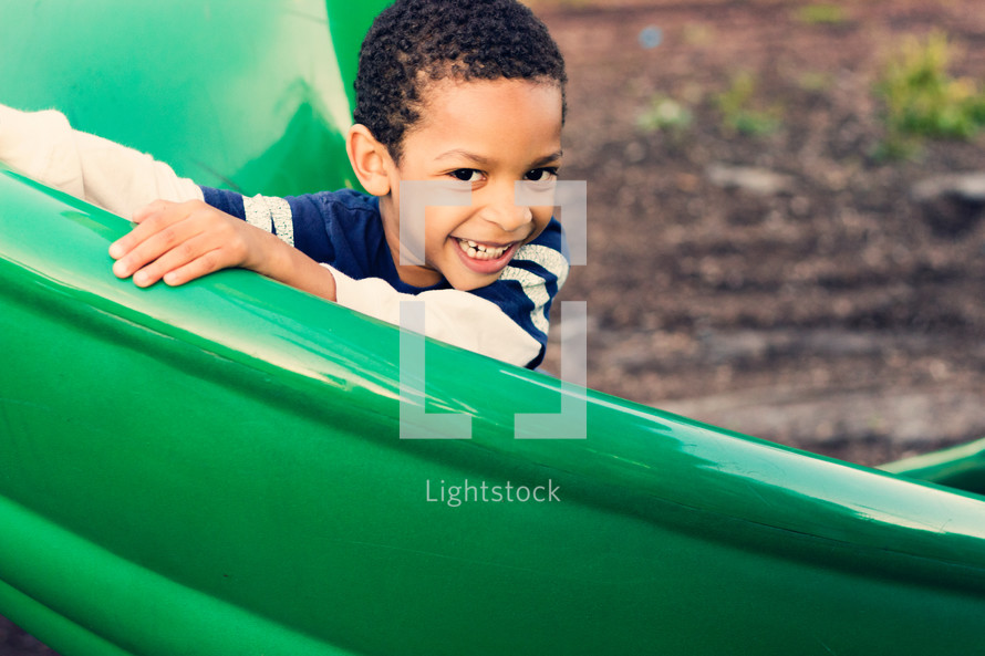 Smiling boy on a playground slide outside.