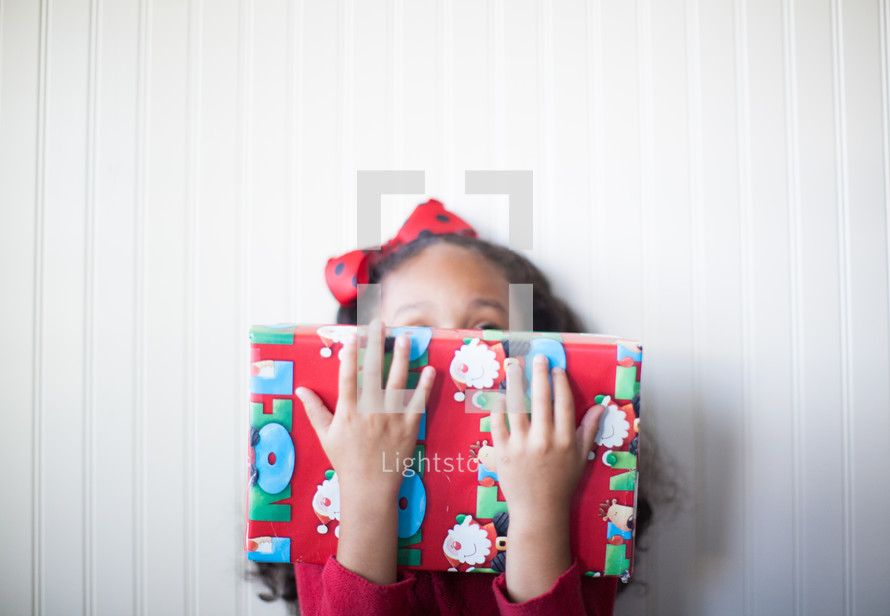 a girl child holding a wrapped Christmas gift 