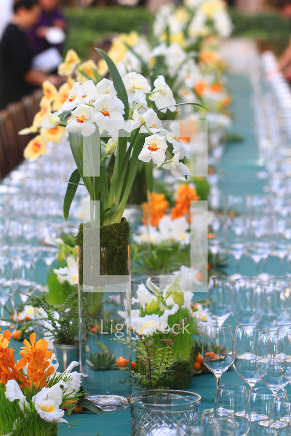 flower arrangements and wine glasses on a long serving table at a wedding