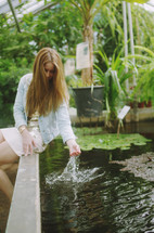 a woman dipping her hand in water in a fish pond 