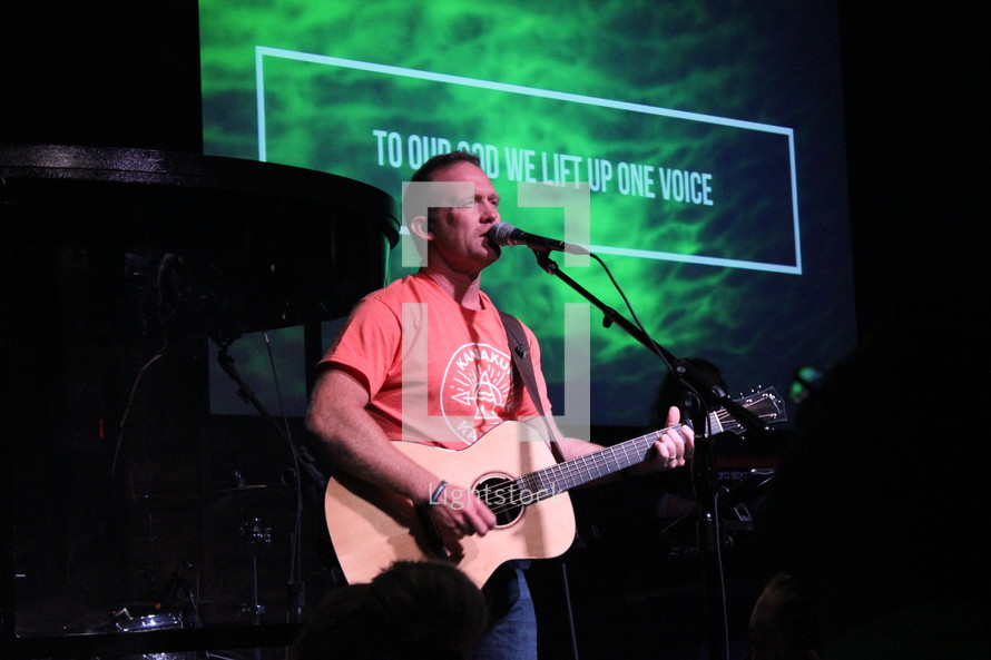 worship leader with a guitar leading a congregation in song 