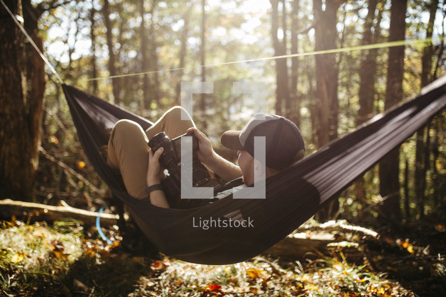 man with a camera resting in a hammock in a forest 