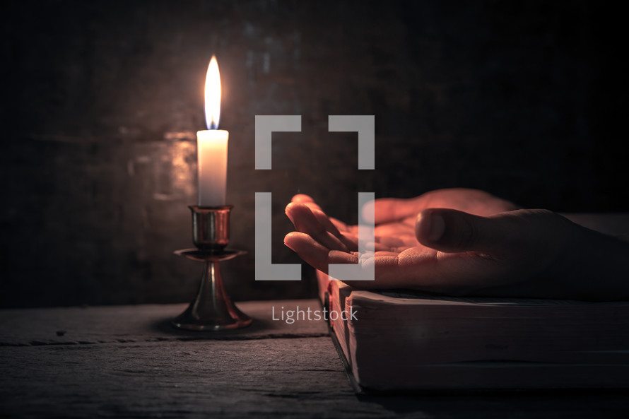 praying hands on a Bible with candlelight 