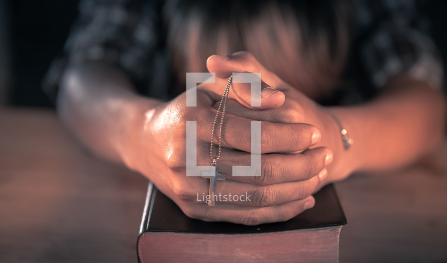a cross necklace in praying hands over a Bible 
