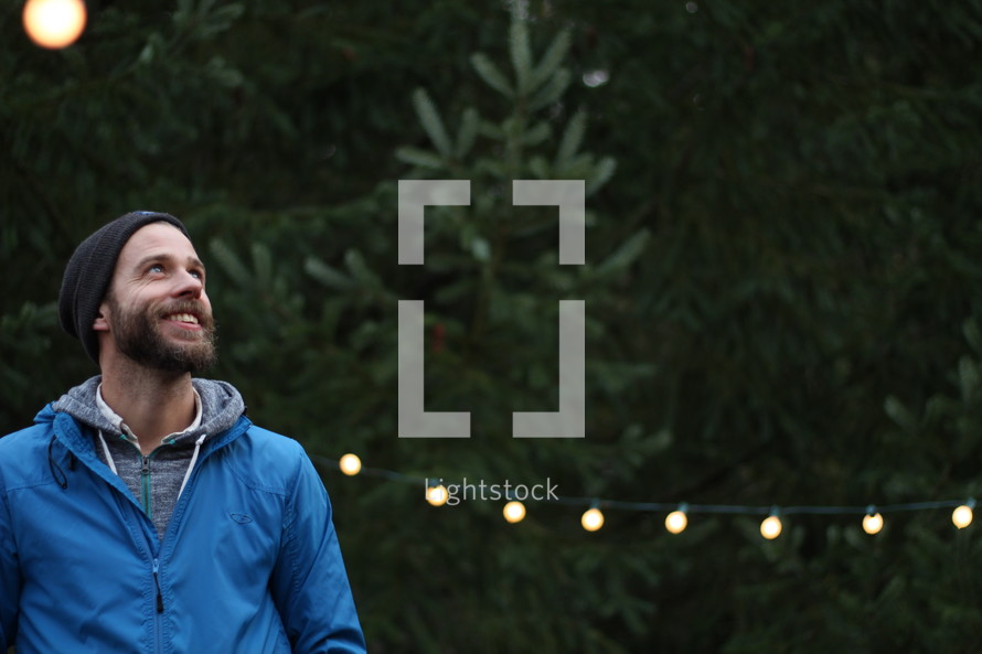 a bearded man standing in a Christmas tree lot
