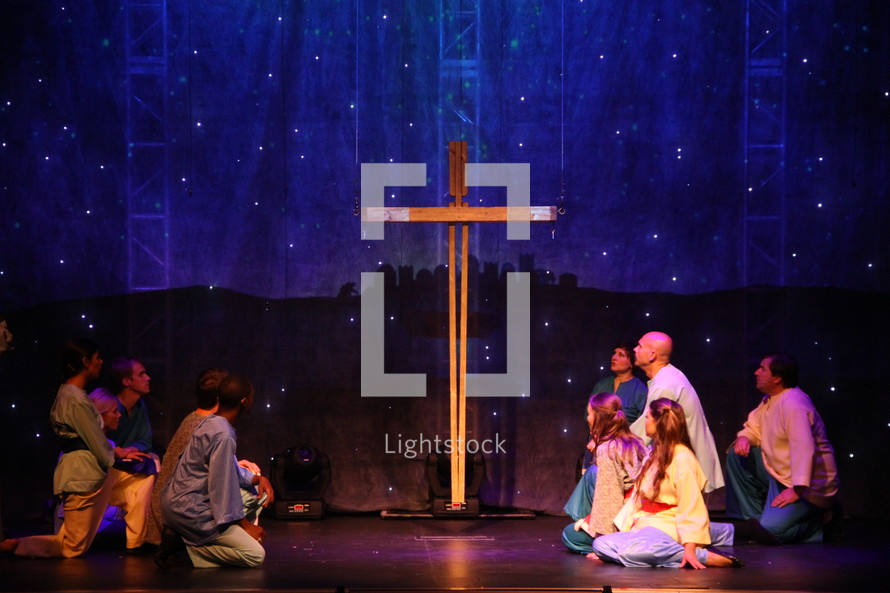 performers on stage kneeling in front of a cross and a scene of Bethlehem 