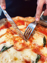 Woman eats with knife and fork a pizza Margherita with mozzarella tomatoes and basil