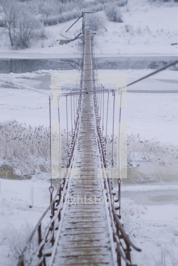 ice and snow on a swinging bridge over a river 
