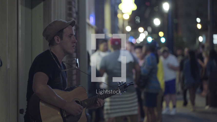street performer playing a guitar on a crowded city sidewalk at night 