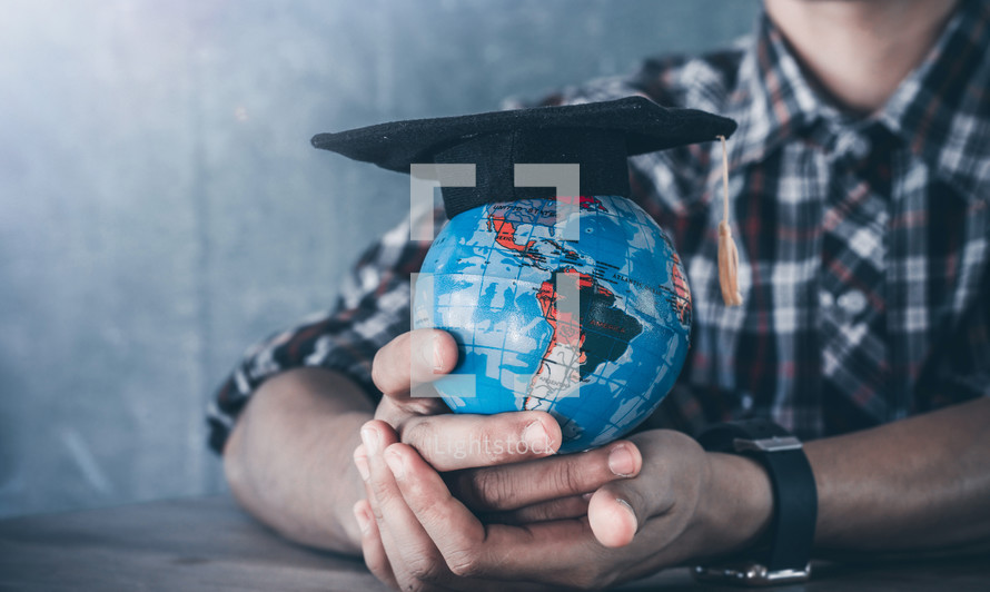 a young man putting a graduation cap on a globe. 