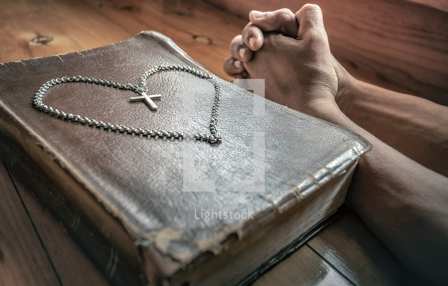 cross necklace in the shape of a heart on a Bible and praying hands 
