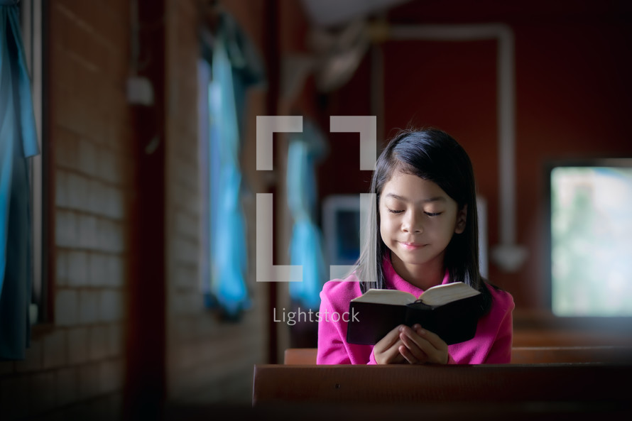 a girl reading a Bible in an empty church 