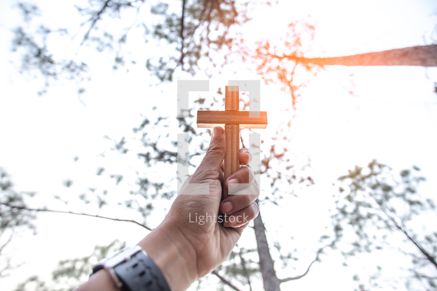 raised hand holding up a wooden cross 