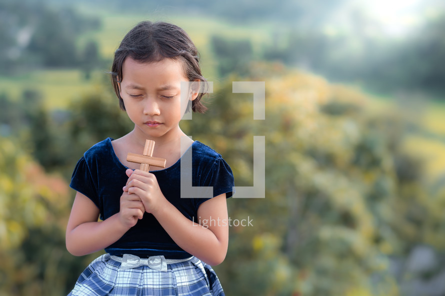 a girl holding a cross praying outdoors 