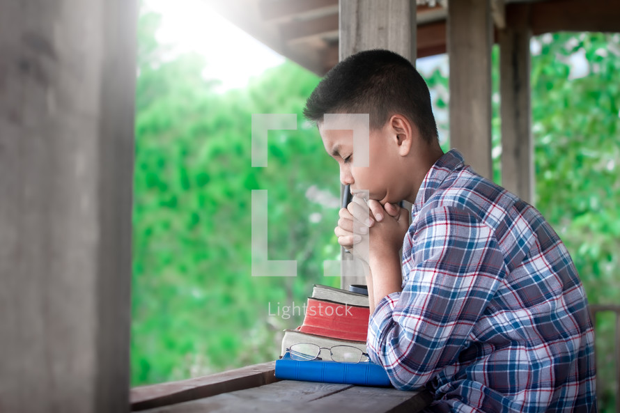 a boy praying outdoors over a stack of Bibles 