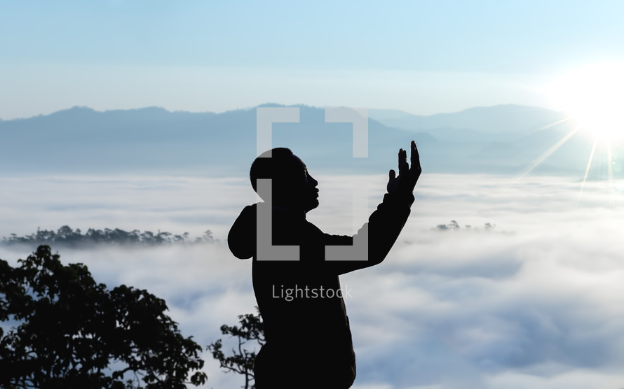 a man standing on a mountaintop in the clouds with raised hands 