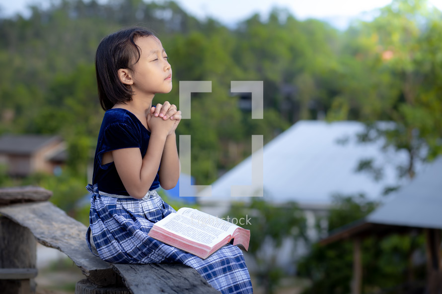 a girl praying with a Bible outdoors 