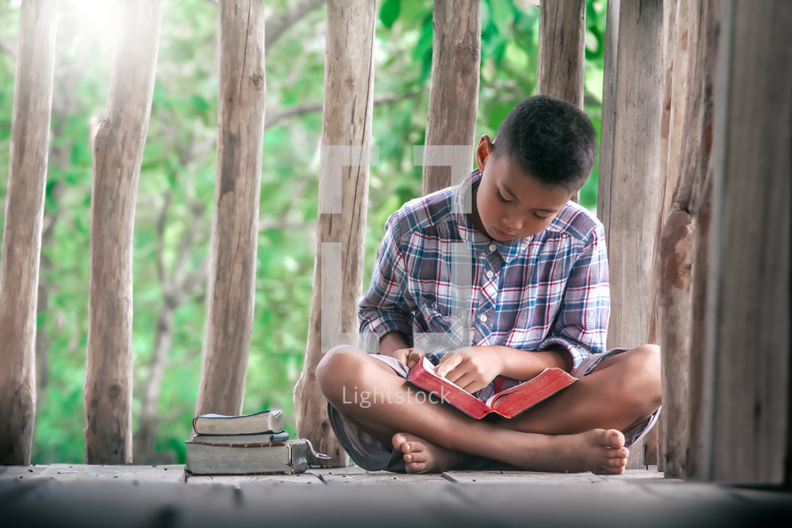 a boy reading a Bible outdoors on a deck 
