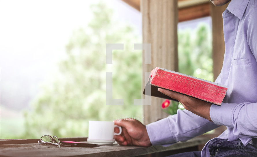 a man sitting at a window in a coffee shop reading a Bible 