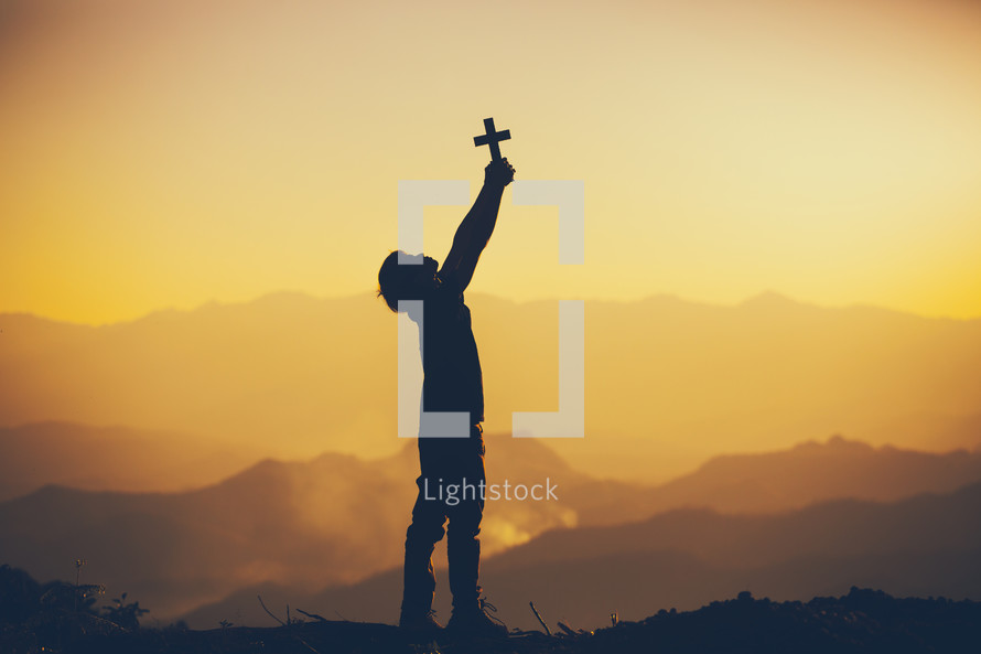silhouette of a boy holding a cross at sunset 