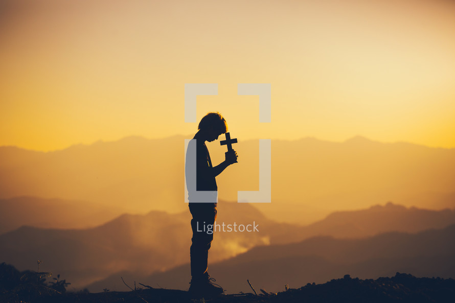 a silhouette of a boy holding a cross at sunset 