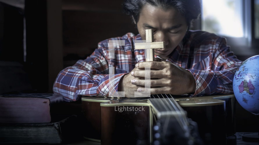 young male playing guitar for worship God on wooden table.
