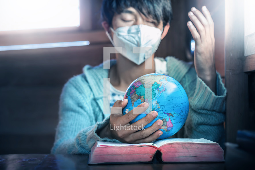 person wearing a face mask with praying hands on a globe 