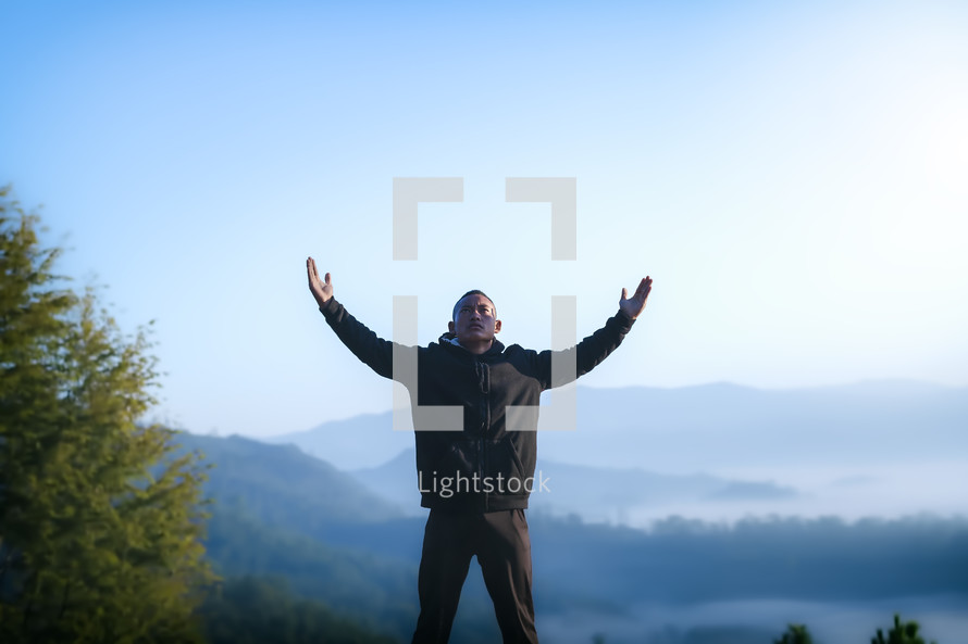 a man with raised hands standing on a mountaintop 
