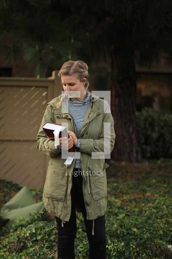 a young woman in a coat holding a Bible outdoors 