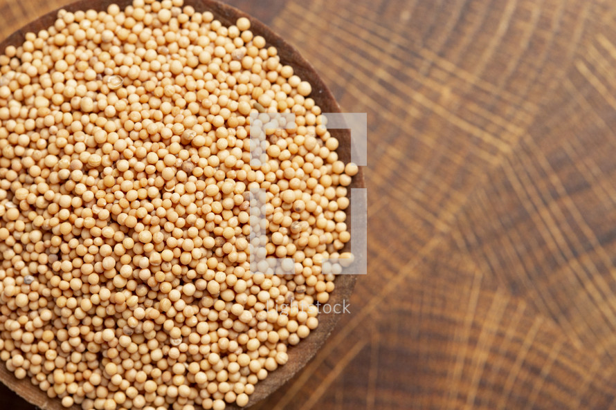 mustard seeds in a wooden bowl on a wood background 
