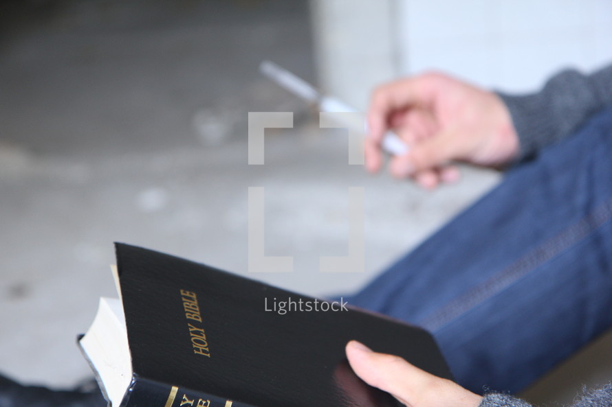 A person holding a Bible in one hand and a writing pen in the other.