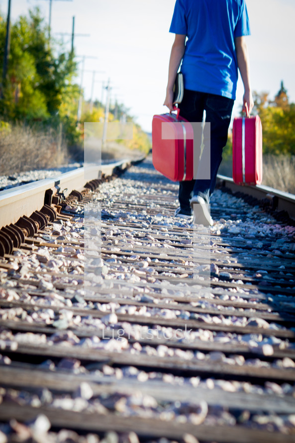 man on railroad tracks walking with luggage 