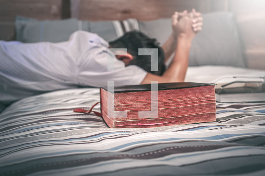 a man kneeling over a bed praying with a Bible 