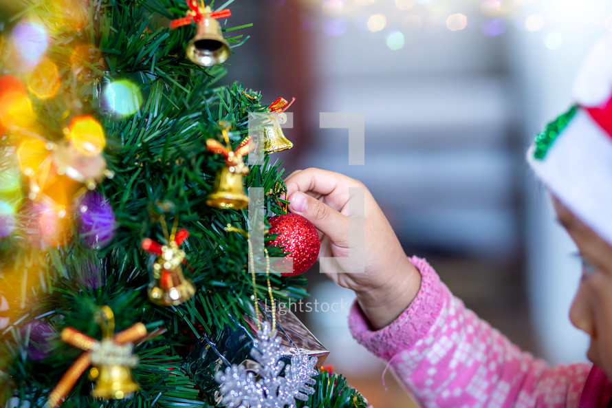 a little girl decorating a Christmas tree 