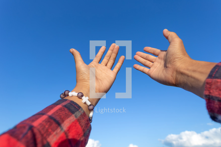 raised hands reaching towards a blue sky 