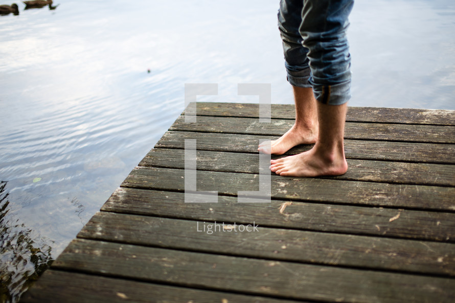 Feet standing on a wooden pier on a lake.