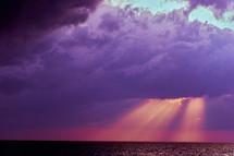 rays of sunlight through purple clouds over the ocean 