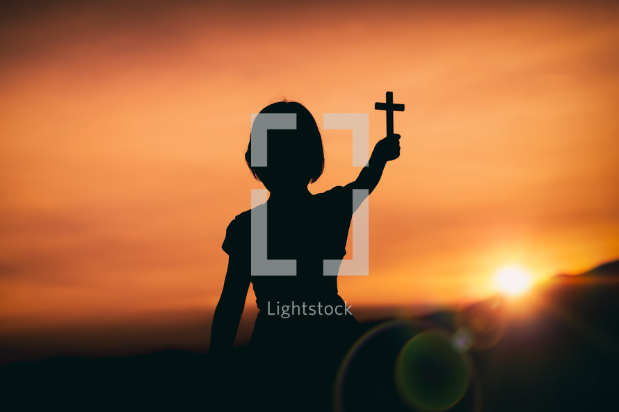 silhouette of a girl holding a small cross 