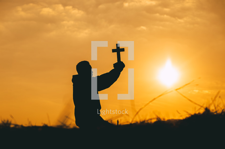 a boy holding a cross at sunset 