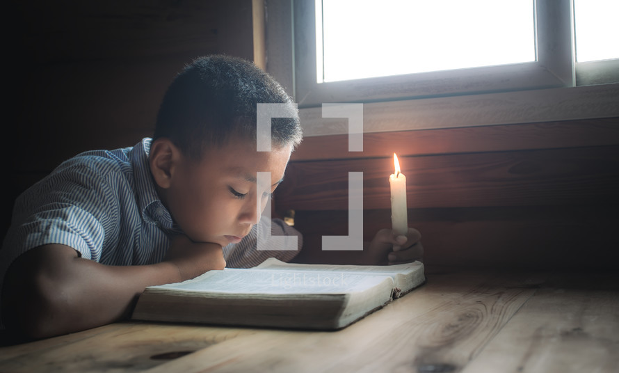 a boy reading a Bible by a window 