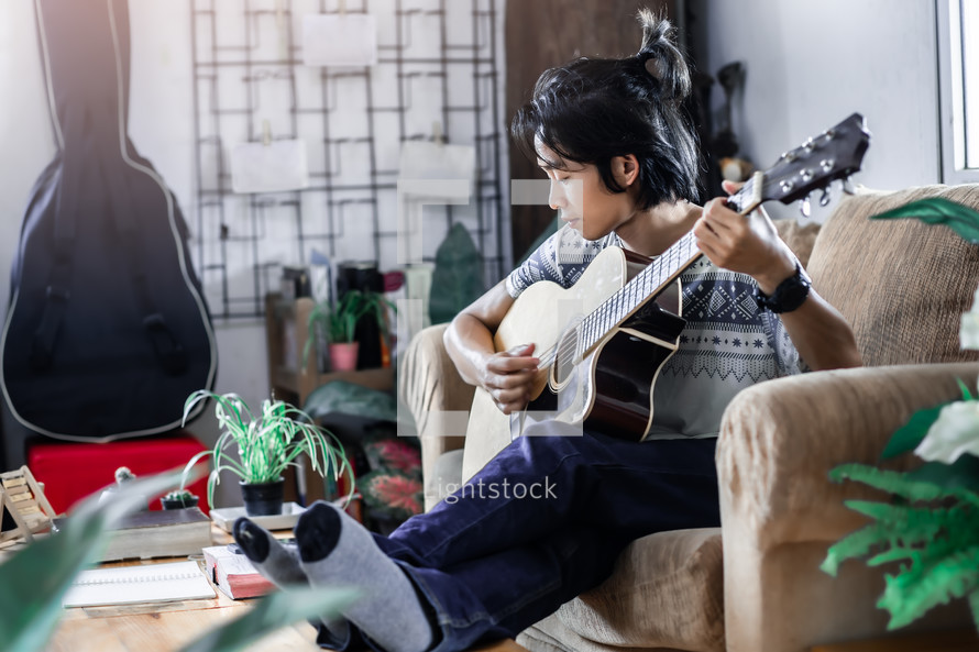 a young man sitting on a couch playing a guitar 