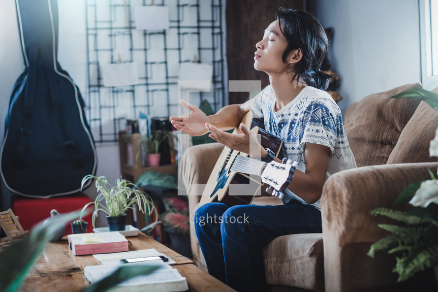 Young male  praying at home next to a guitar 