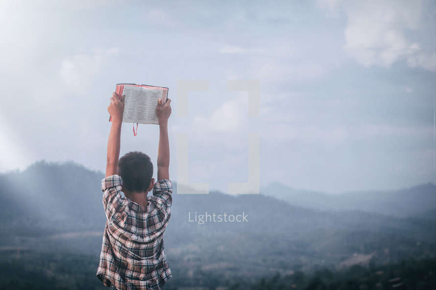 a boy holding up a Bible outdoors 