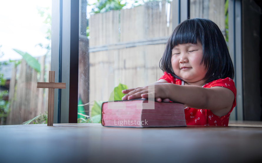 a little girl praying over a Bible 