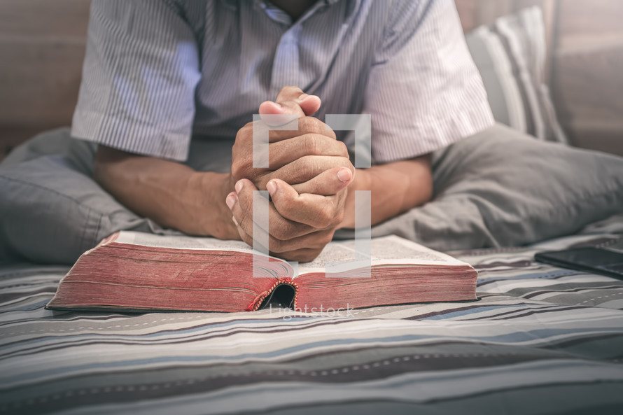 praying hands over a Bible in bed 