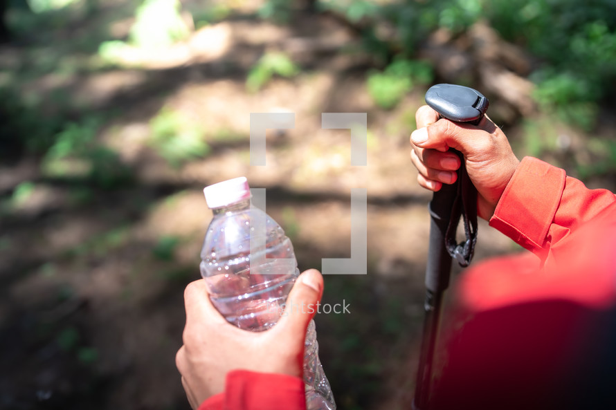 Close up hand hiker man holding bottle of water and hiking poles in forest