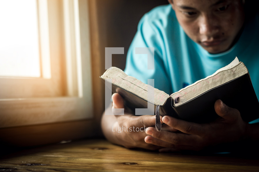a man reading a Bible by a window 